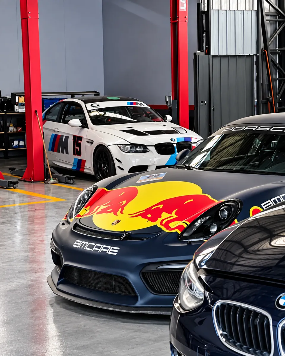 Porsche de competición con la marca BMCARE y BMW M3 de carrera en el taller BMCARE Motorsport